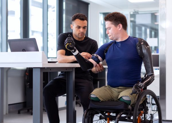 Man assisting person in a wheelchair with prosthetic arms