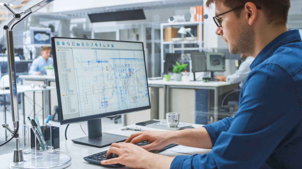 Man in front of a monitor displaying technical drafts