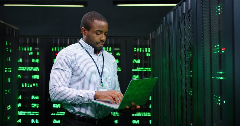 Man standing holding laptop in a computer server room