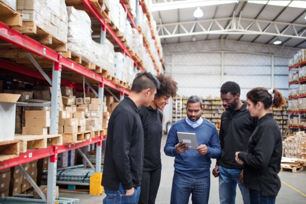 Group of individuals in a warehouse standing together looking at a tablet