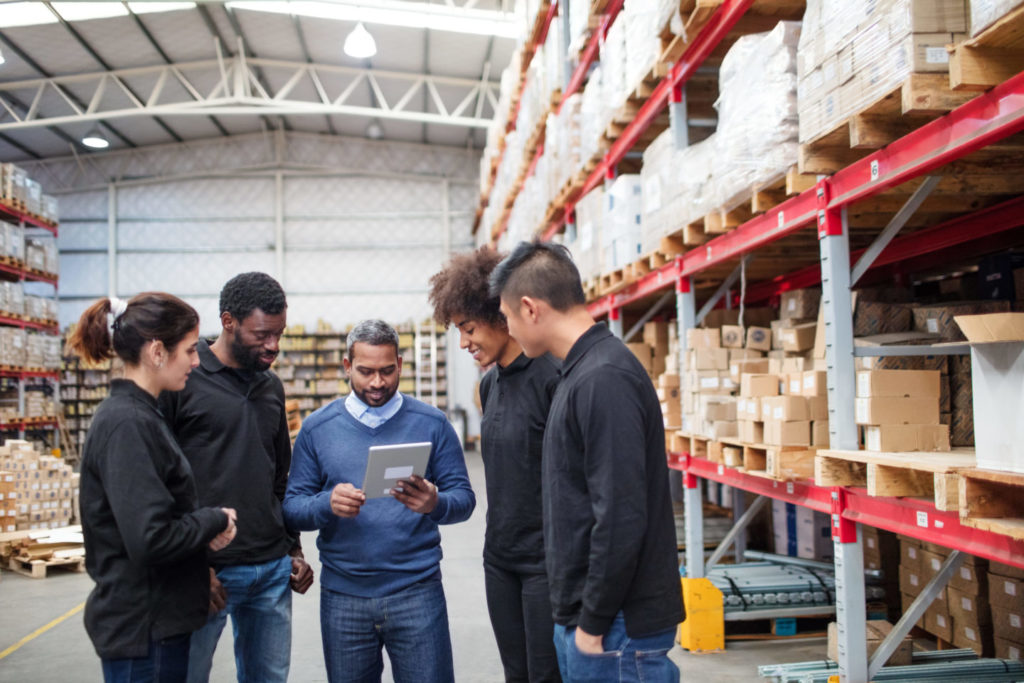 Group of individuals in a warehouse standing together looking at a tablet