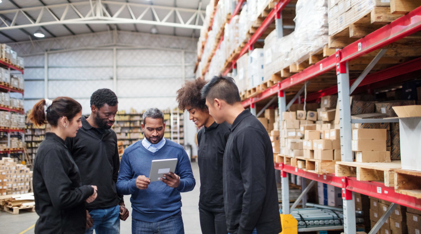 Group of individuals in a warehouse standing together looking at a tablet