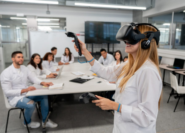 Group of people sitting down in labcoats observing a woman with a VR headset