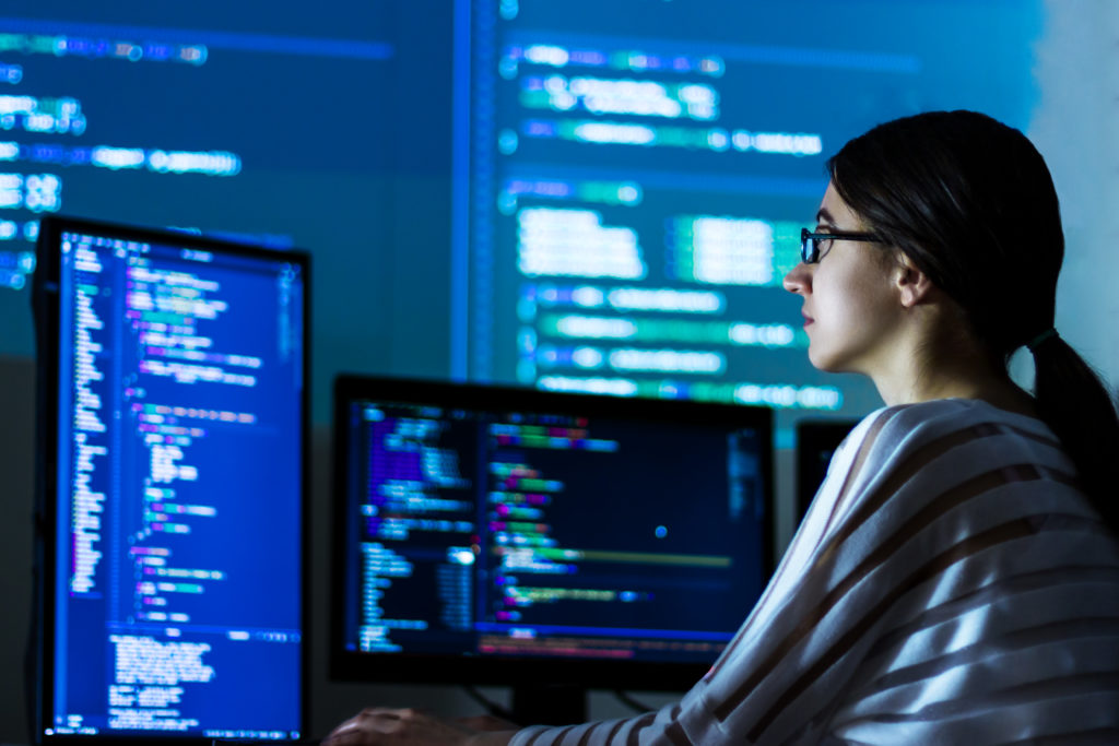 Woman in front of multiple screens displaying code